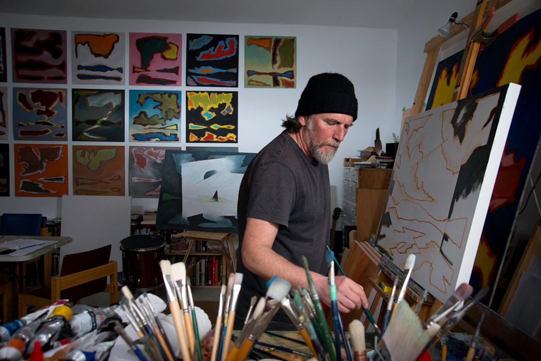 Artist John Climenhage finds the details very important as he works a new work on a large canvas. Behind him on the wall are rows of square paintings about one foot square. They show some of his newest abstract ideas in this portrait by photographer Mike Taylor.