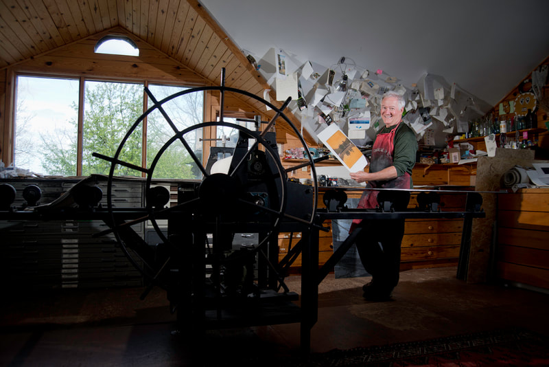 A smiling man, holds a print he recently made on his printing press.