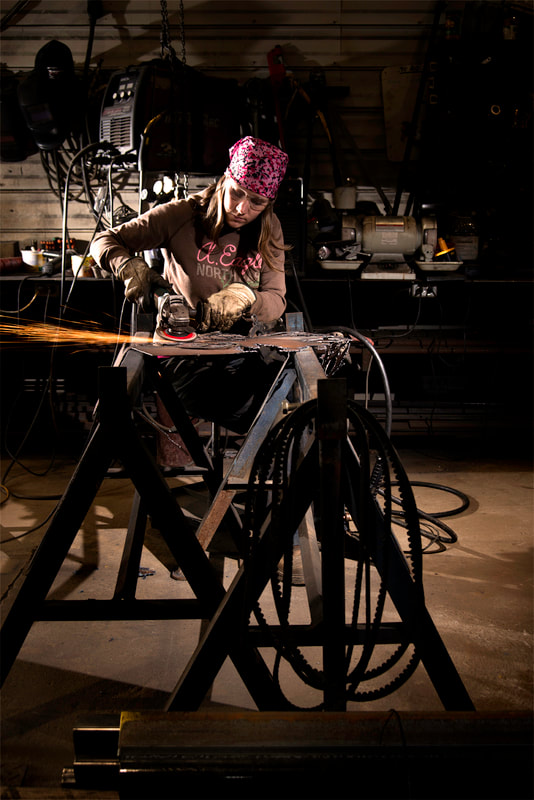 A woman with a pink head scarf, works with some welding equipment in her workshop.