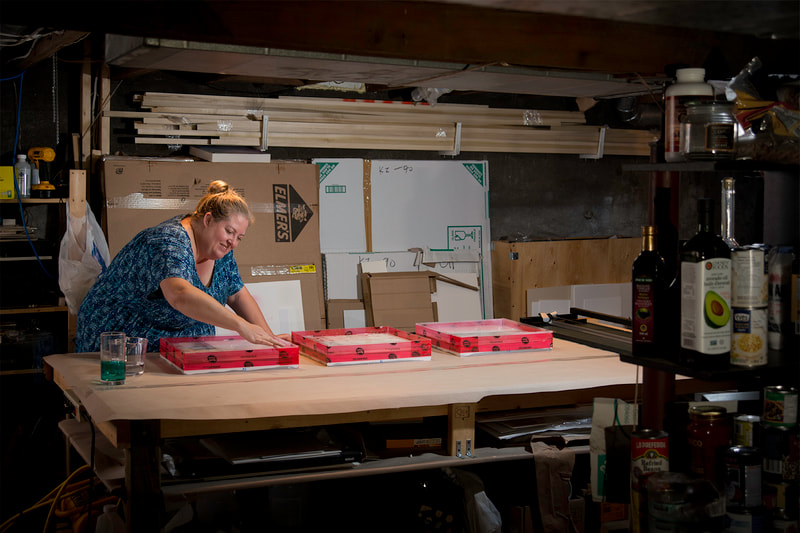 A woman in a blue top works her artwork in her basement work studio